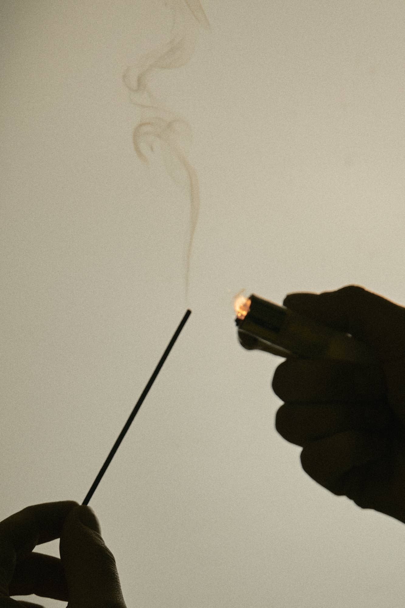 Hand lighting a incense stick with a lighter against a plain background