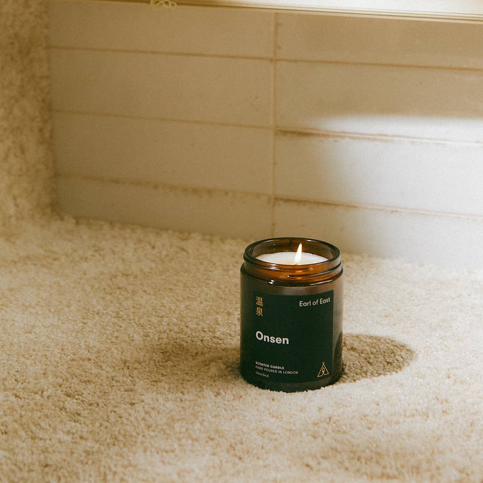 Candle labeled 'Onsen' in a glass jar on a carpeted floor.