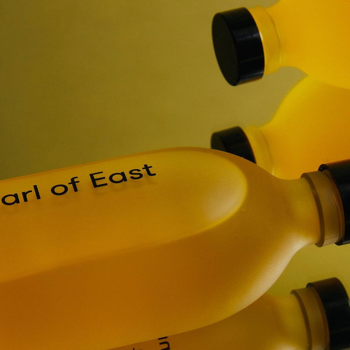 Close-up of yellow bottles with black caps on a yellow background, featuring the text 'arl of East'.