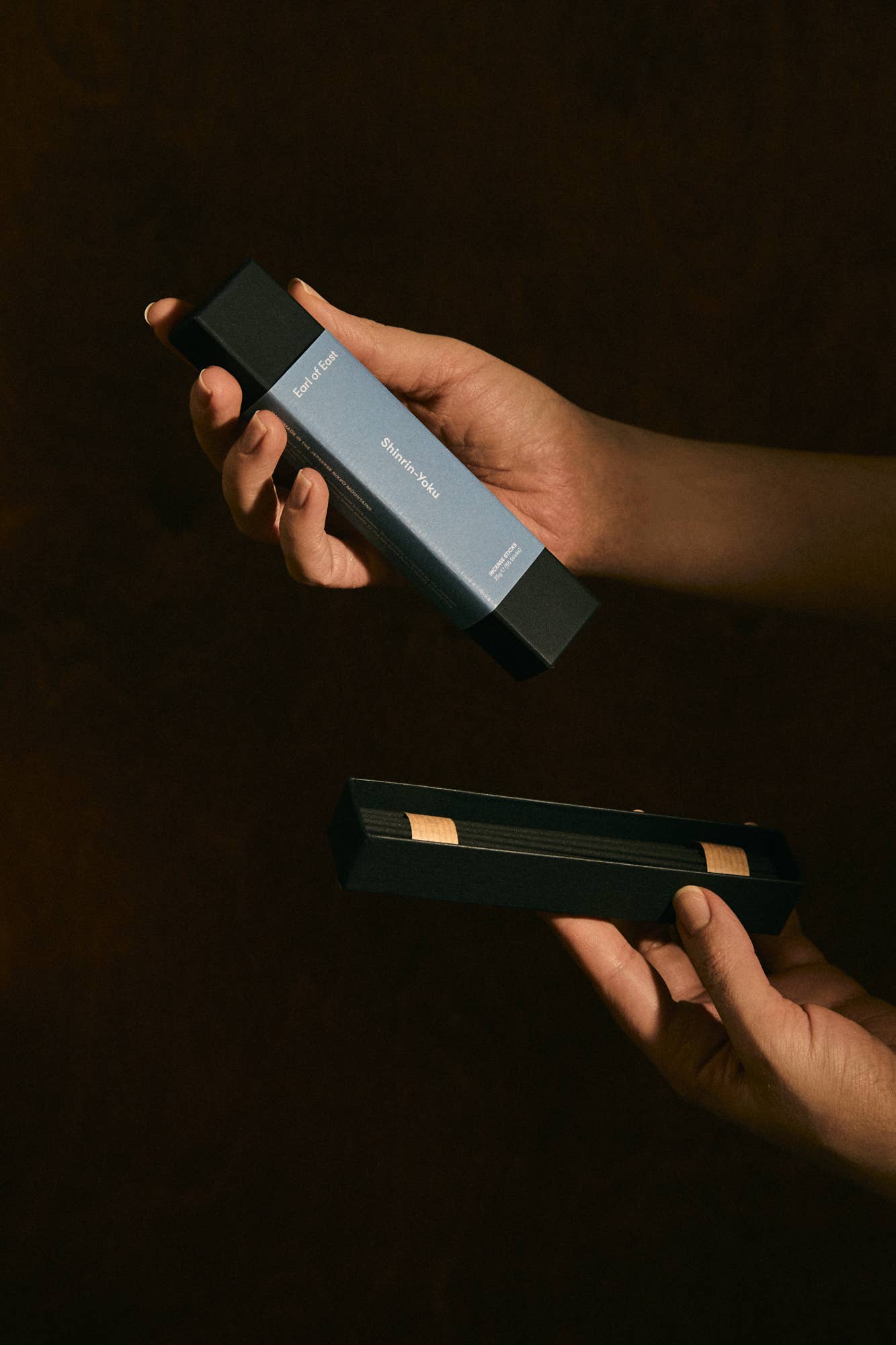 Two hands holding a black rectangular object against a dark background