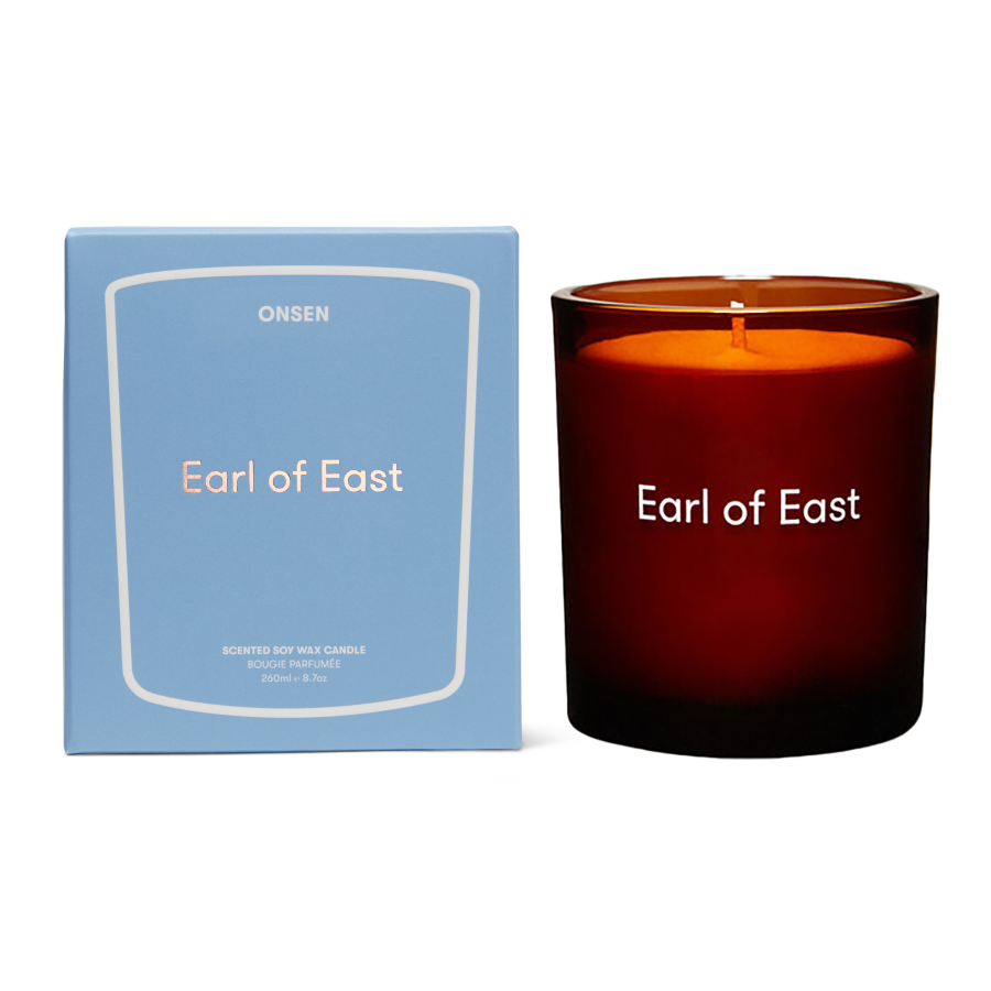 An Onsen 'Earl of East' scented soy wax candle in an amber glass jar next to its light blue packaging box, shown on a clean white background.