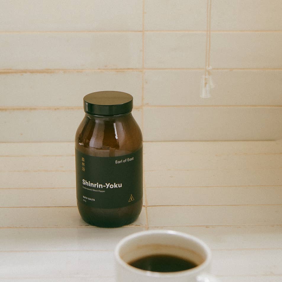 Brown bottle labeled 'Shinrin-Yoku' on a tiled bathroom counter with a cup of coffee.