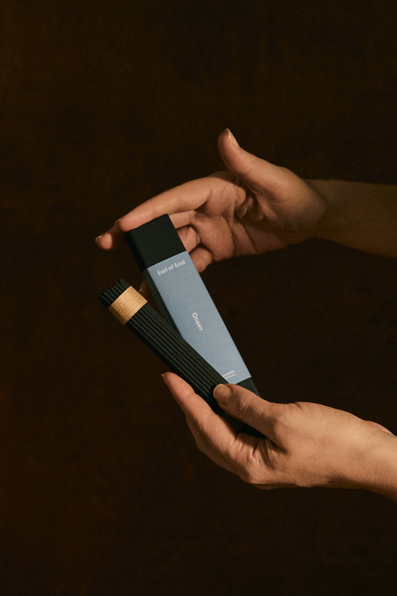 Two hands holding a black and blue hairbrush against a dark background