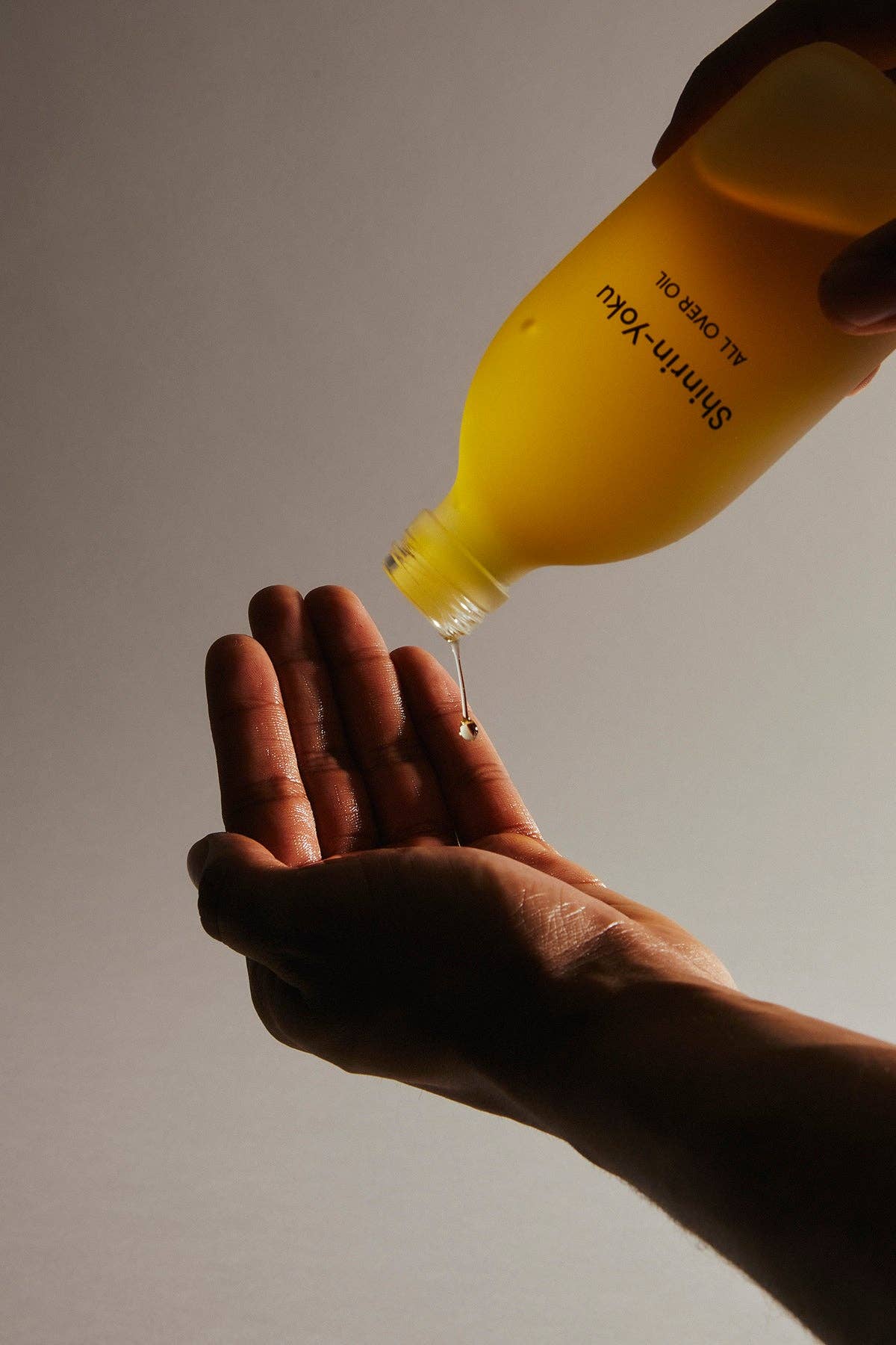 Yellow bottle pouring liquid into a hand against a neutral background