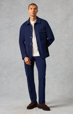 Man wearing a navy blue jacket and pants with a white shirt underneath on a gray background