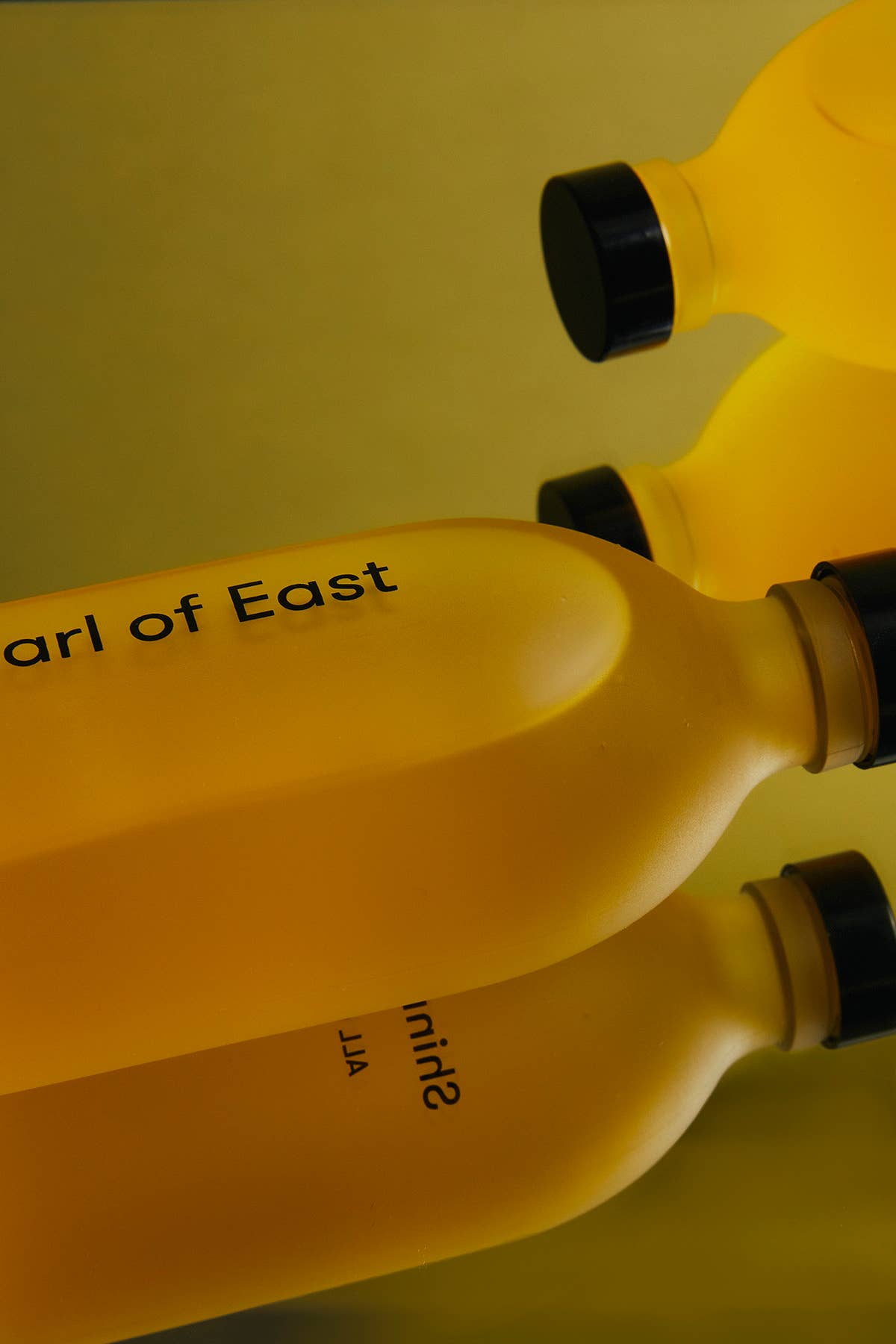 Two yellow bottles with black caps on a yellow background