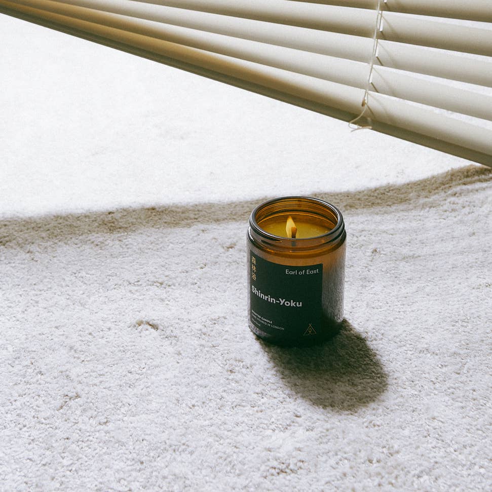 Candle in a glass jar with a label on a carpeted floor.